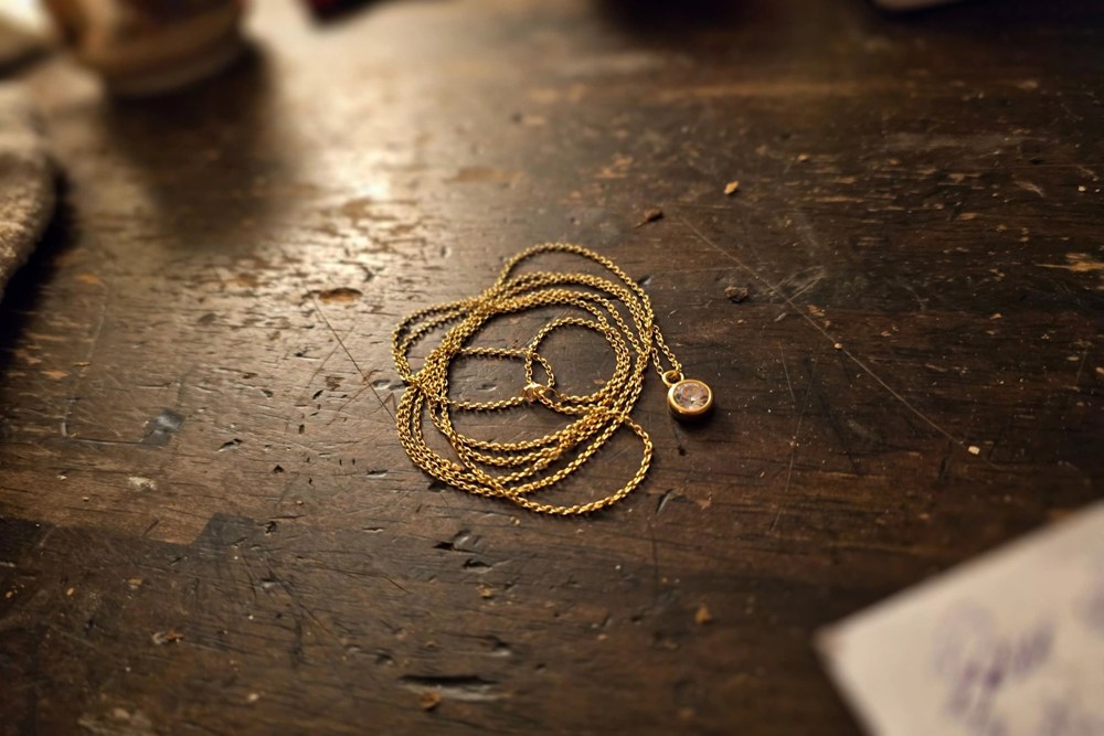 The original phone photo: a gold necklace coiled on a scratched wooden table